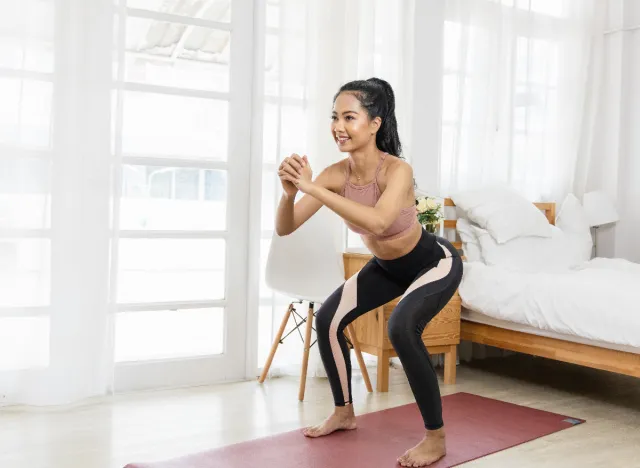 woman doing squats as part of at-home 30-day boot camp workout to flatten your belly