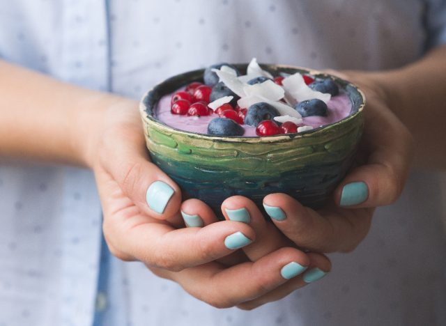 woman's hands holding bowl of yogurt topped with fresh fruit