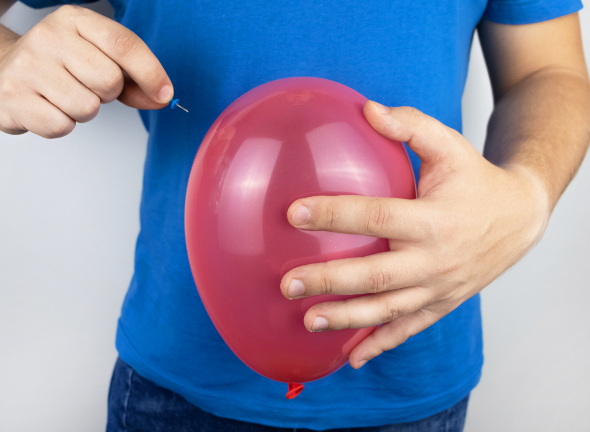 deflate balloon belly bloat concept, man holding pink balloon with push pin