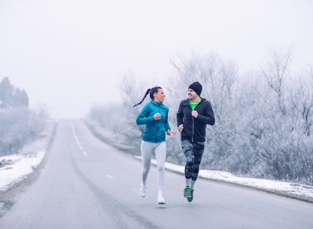 fit couple on a winter run, snowy backdrop, how to get out of winter workout rut