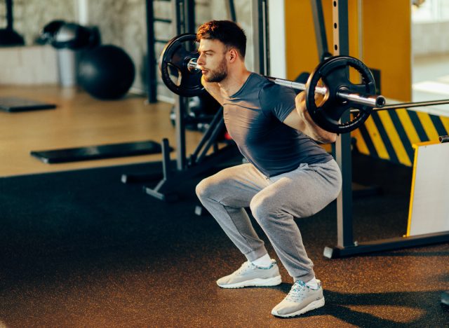fit man performing barbell squats at gym