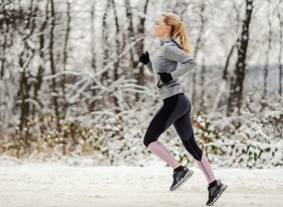 blonde fitness woman running through the snow, demonstrating how to get back into shape after a break