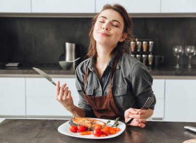 happy woman eating fish and tomatoes