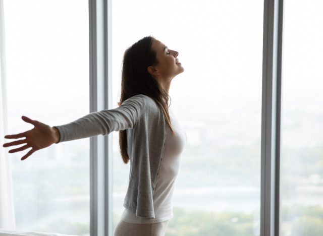 happy woman soaking up morning light by bright windows