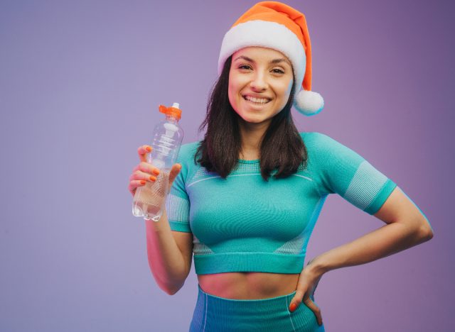 fitness woman wearing santa hat and holing water bottle, concept of easy fitness habits to follow over the holidays
