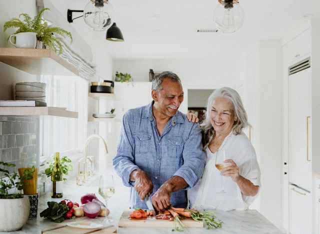 mature couple in kitchen chops veggies and prepares a healthy meal