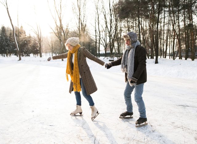 mature couple ice skating outdoors on frozen lake, winter weight loss activities concept