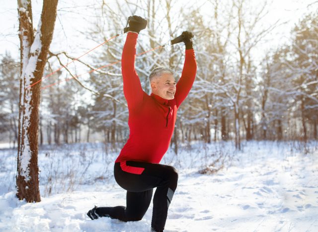 mature man in snow doing bodyweight exercises and uses resistance band