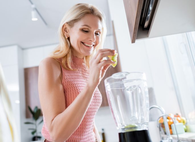 mature woman making healthy smoothie in kitchen, transform your body after 60 concept