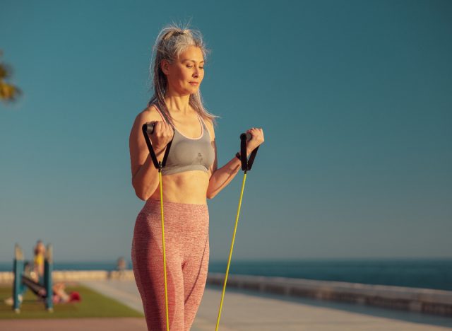 Mature woman exercising with resistance band by the beach