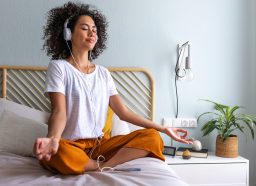 relaxed woman listening to brown noise on headphones and meditating in bed