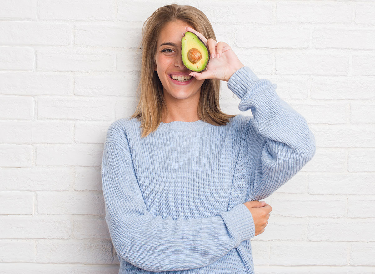 Beautiful,Young,Woman,Over,White,Brick,Wall,Eating,Fresh,Avocado