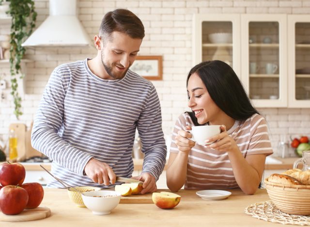 Couple slicing apples and drinking tea in the kitchen.