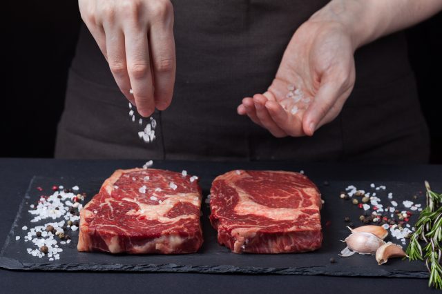 Chef sprinkles salt on raw steak