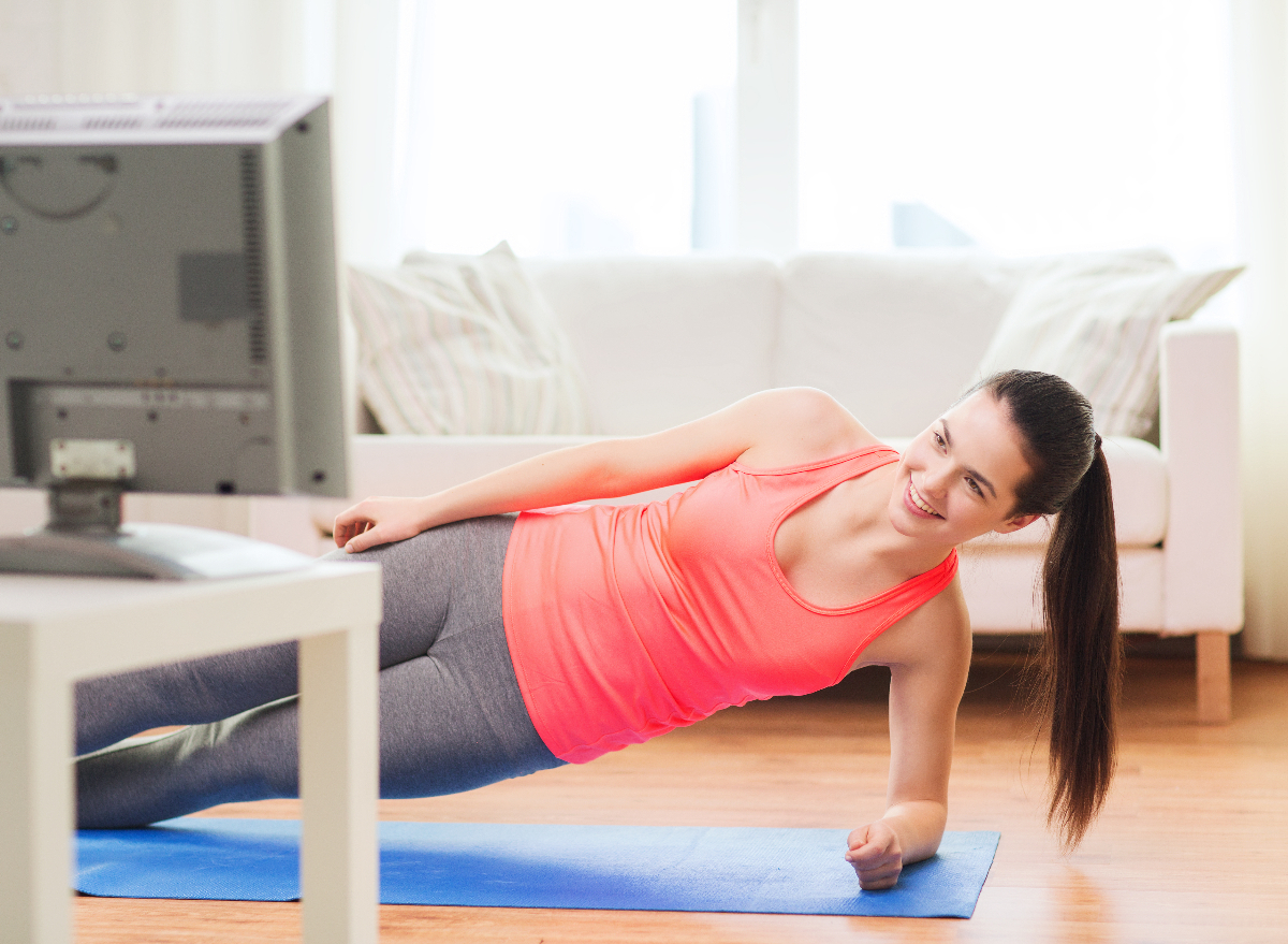 woman demonstrating side planks in her at-home workouts while streaming Netflix in bright apartment