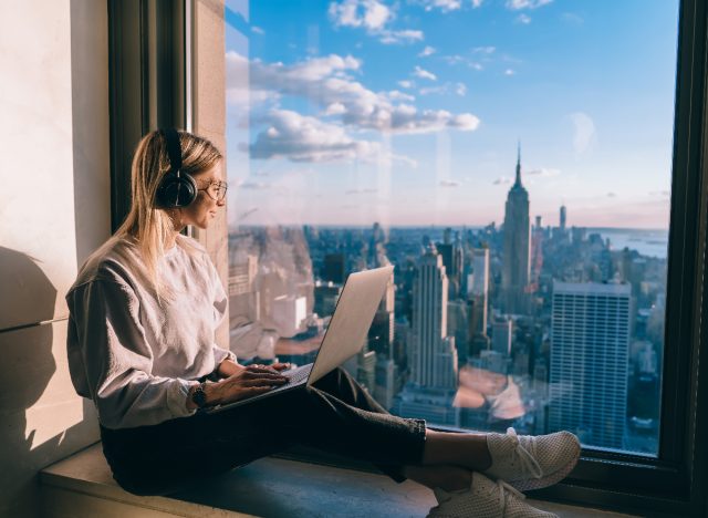 woman looking out at city view while listening to brown noise and working on laptop