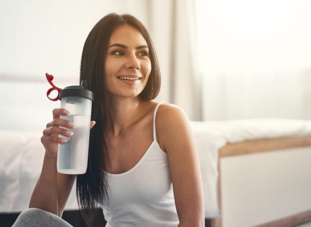 woman drinking water bottle in bright bedroom, concept of how to burn calories while watching TV