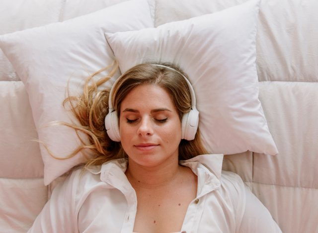 woman with eyes closed on bed listening to one of the best meditation apps for holiday stress