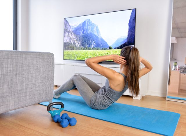 woman doing sit-ups on mat in front of her TV while watching movie