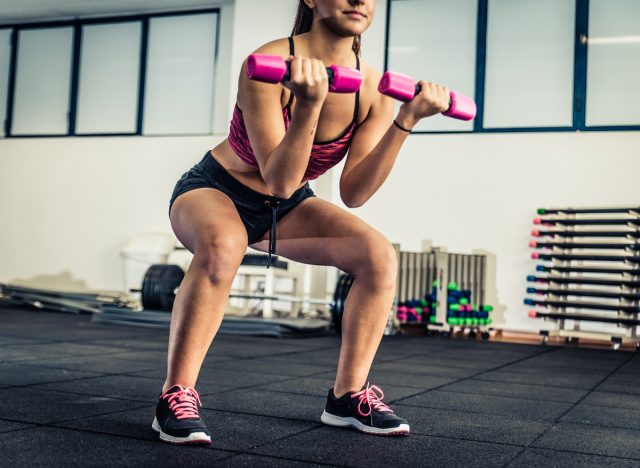 woman holding dumbbells doing a squat and demonstrating workout for rapid weight loss at gym