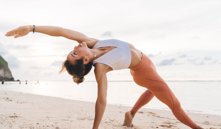 woman doing yoga on the beach, demonstrating how to age-proof your back
