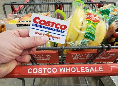 A hand holding a Costco Membership card on a cart in Costco