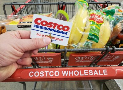A hand holding a Costco Membership card on a cart in Costco