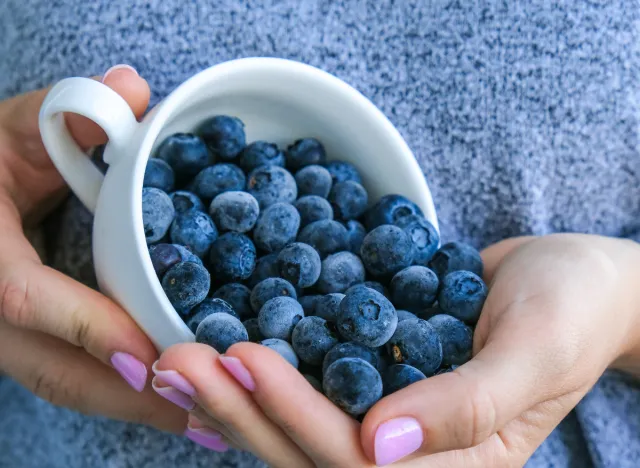 close-up woman pouring cup of blueberries into hand, the best superfoods for a flat belly