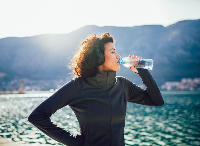 fitness woman drinking water on a run, concept of everyday habits for a flatter stomach that are easy
