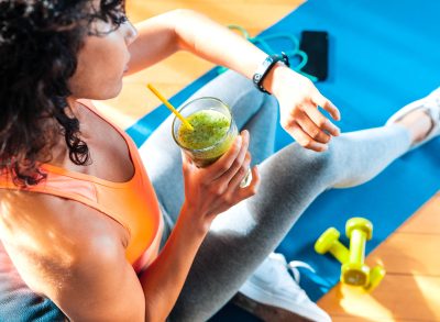 fit woman holding green smoothie and checking fitness tracker on mat, concept of worst weight loss tips to follow