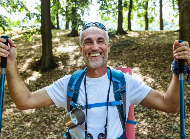 happy mature man holding walking sticks on outdoor hike