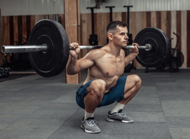 man performing barbell squats at the gym