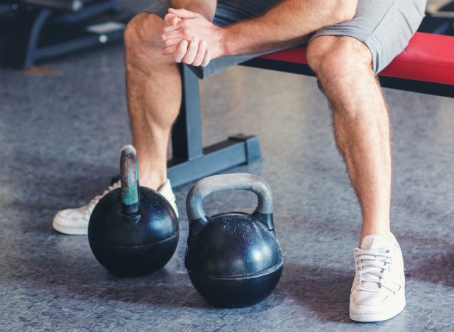 man sitting on workout bench with kettlebells, concept of how to get rid of moobs