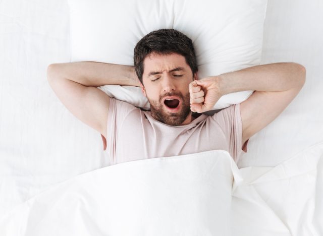 ベッドで疲れ果てたあくびをする男性