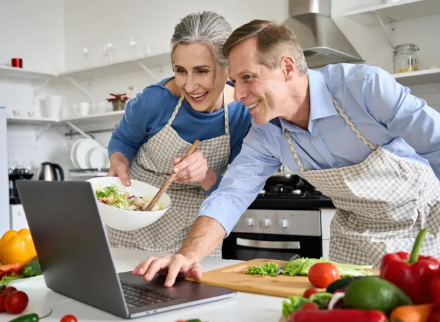 mature couple cooking part of weight loss program, looking at recipe on laptop