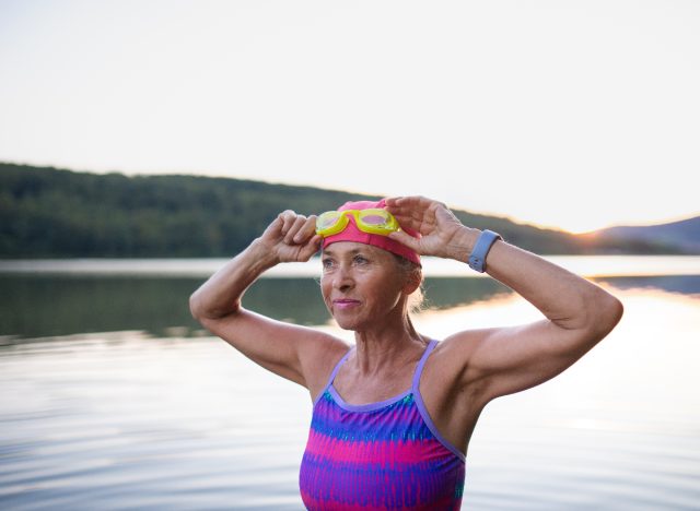 mature fit woman putting on goggles by lake, demonstrating cardio exercises to keep your heart young