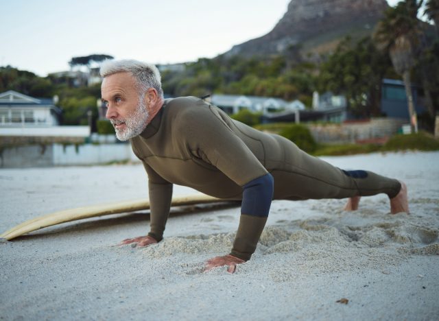 mature man doing beach pushups muscular endurance exercises in a wet suit