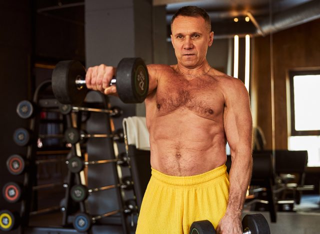 mature man lifting heavy dumbbells at the gym, concept of exercise habits that destroy your back after 50