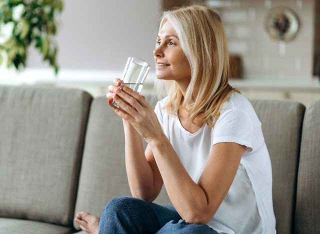 mature woman sitting on couch drinking a glass of water