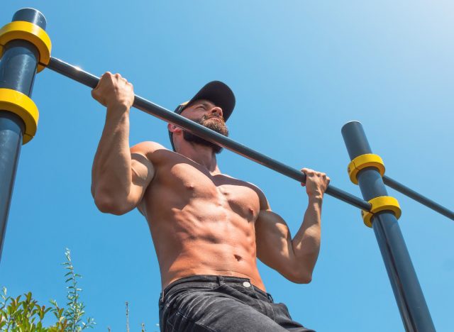 muscular man doing reverse pull-ups outdoors
