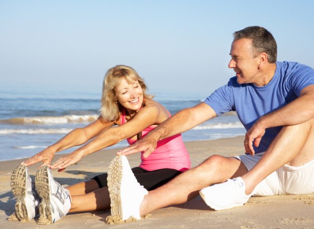 senior couple stretching on the beach, concept of healthy lifestyle habits that are prematurely aging you