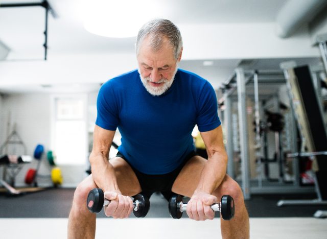 senior man doing leg-strengthening exercises squats with dumbbells at the gym