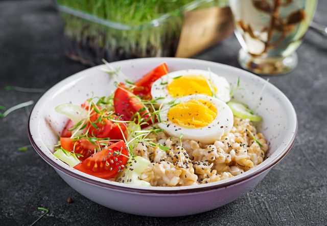 Oatmeal breakfast with boiled egg, cherry tomatoes, celery, and microgreens.  Healthy balanced food.