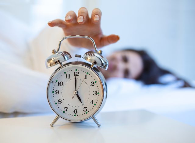 woman lying in bed turning off alarm at 5 am