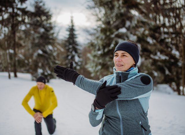 two mature skiers stretching on snowy slopes after skiing