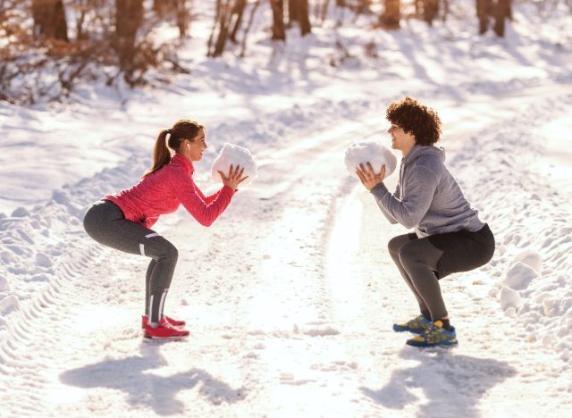 sporty couple does squats in the snow, demonstrating movement snacking quick workout trend