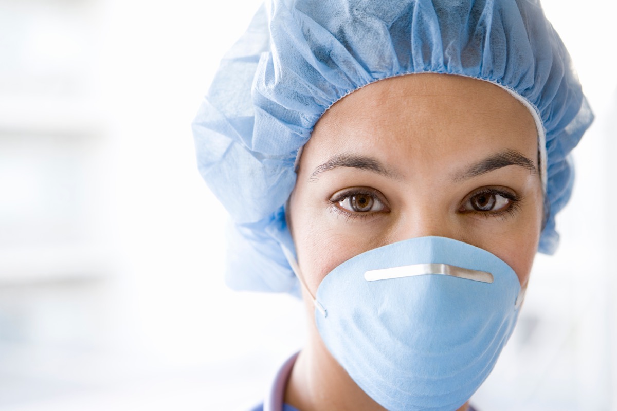 Young,Female,Nurse,At,Camera,Wearing,Surgical,Mask,And,Scrubs
