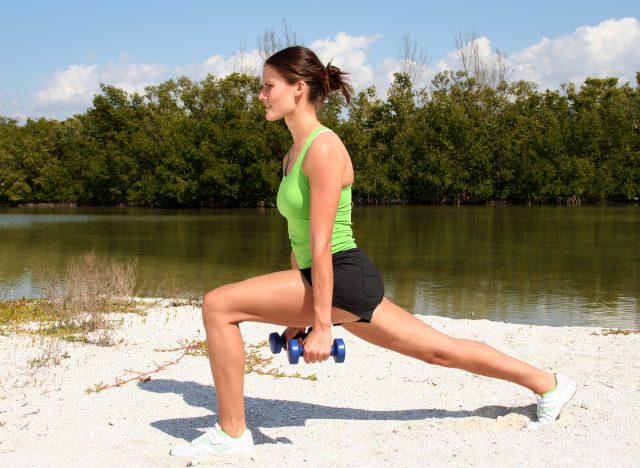 woman doing dumbbell lunges on beach as part of 30-day workout