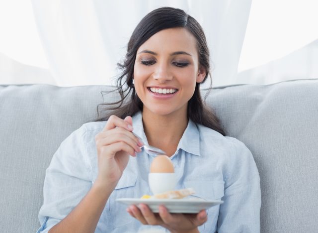 happy woman at home enjoying hard-boiled egg in bright living room