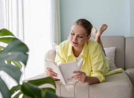 woman reading self-help books in her bright home on a couch